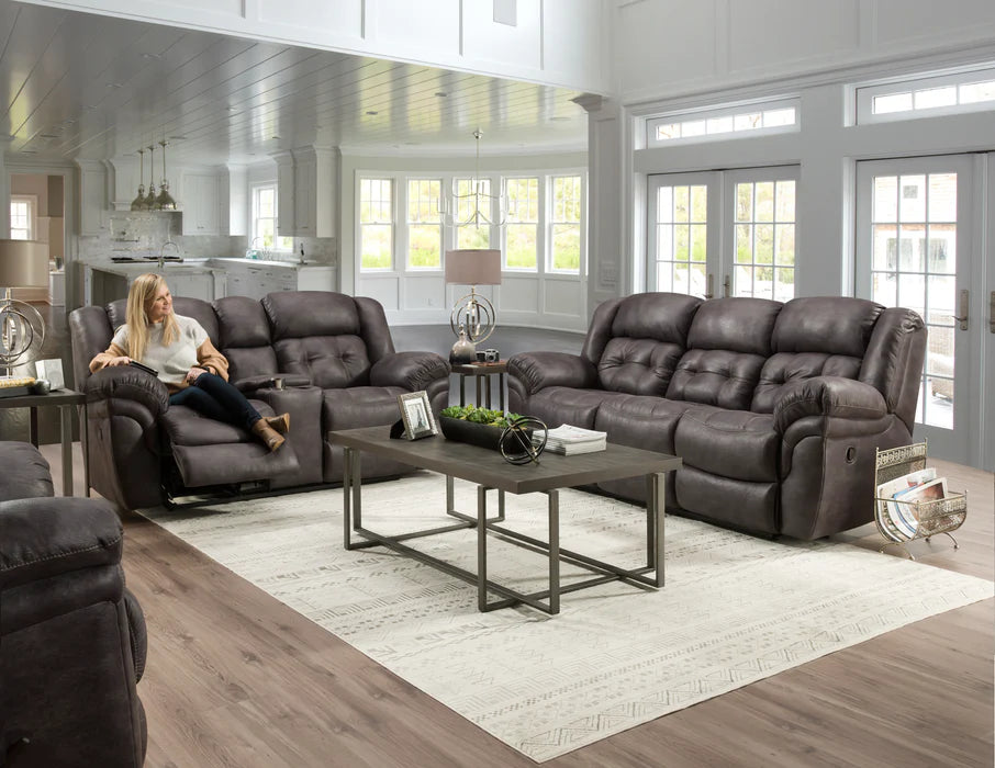 Living room with dark gray reclining sofa set and woman sitting on a chair.